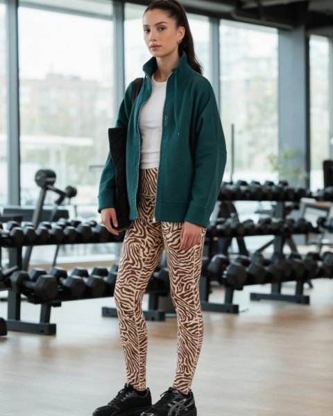 Junge Frau in Leo-Leggings und grüner Sweatjacke im Fitnessstudio